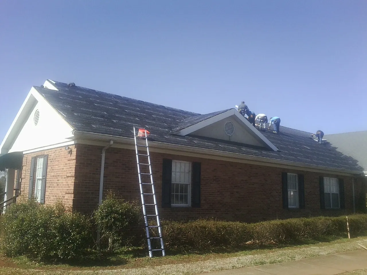 Crew tearing shingles off a brick ranch roof with a ladder set — Emergency Roof Repair work by our crew in Parrish