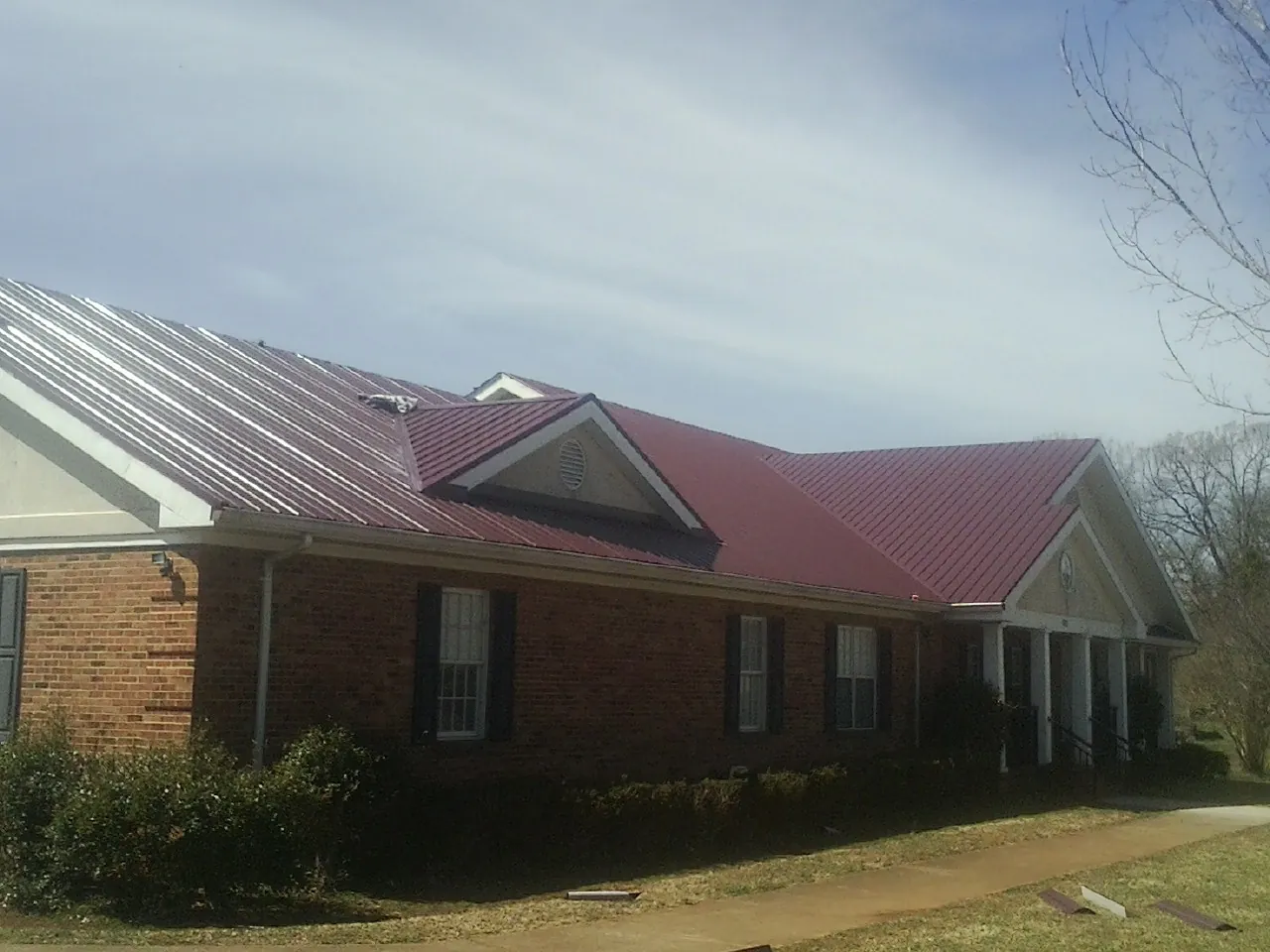 Red metal roof with gabled entries on a long brick building, from a Hail Damage Roof Repair job in Parrish