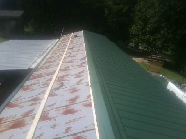 Old rusted panels beside newly installed green metal roofing — Wind Damage Roof Repair by Roofing Brothers in Parrish