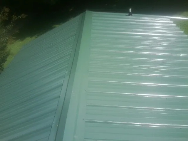 New green metal panels meeting at the ridge of a roof — Flat Roof Repair work by our crew in Parrish
