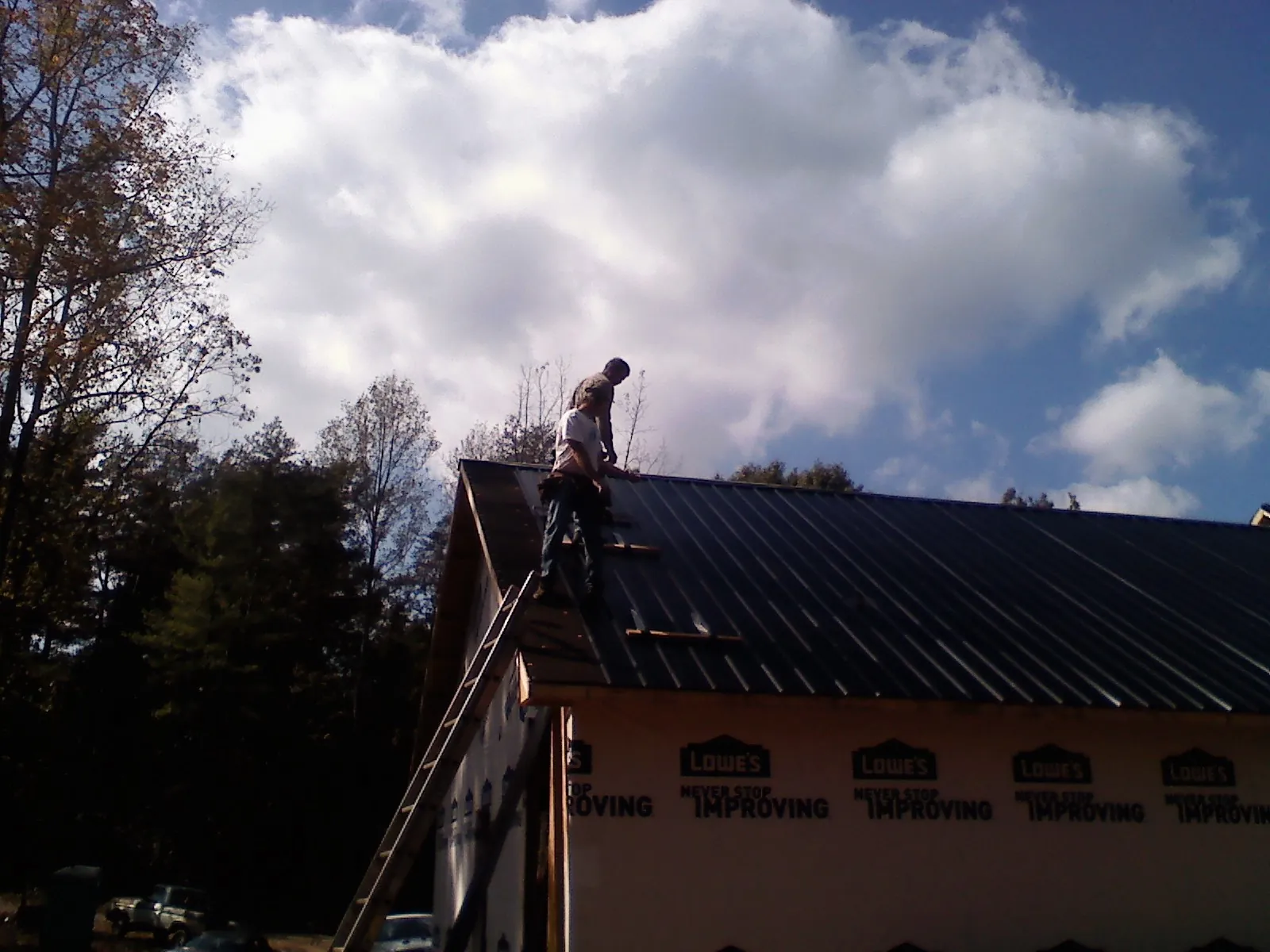 Roofer fastening dark metal panels high against a cloudy sky, from a Roof Inspection job in Parrish