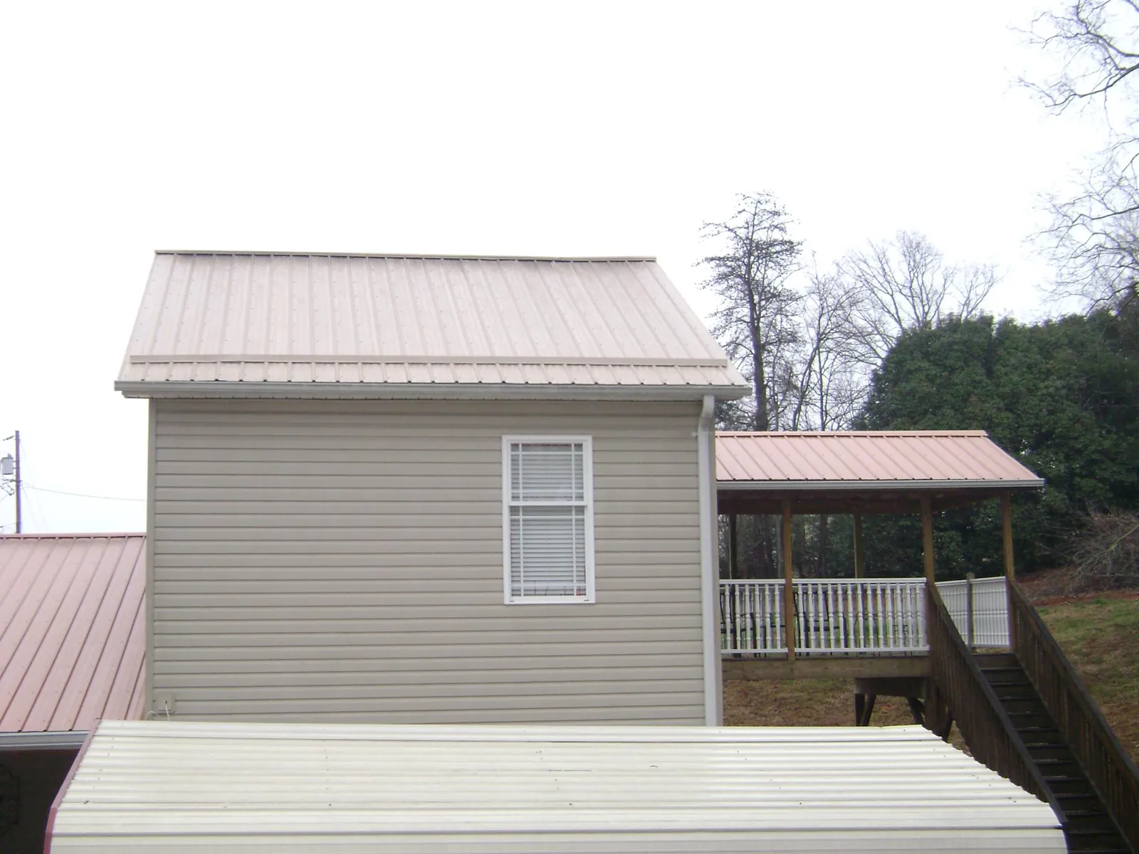 Tan metal roofs on a two story addition and attached porch, from a Roof Replacement job in Parrish